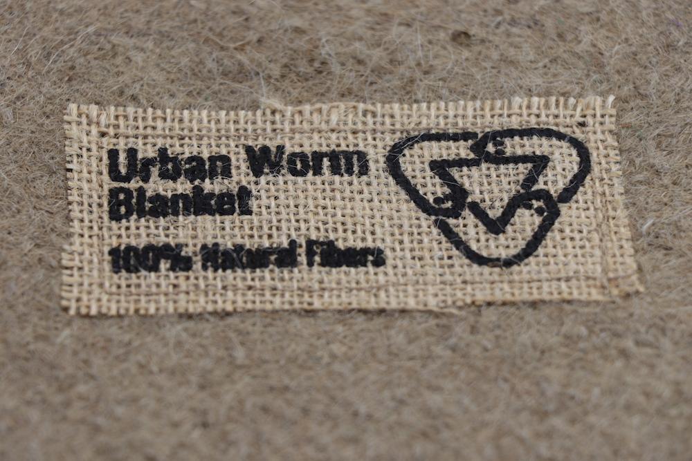 Close-up of the Urban Worm Blanket label on natural jute fiber used as breathable worm bedding for vermicomposting.