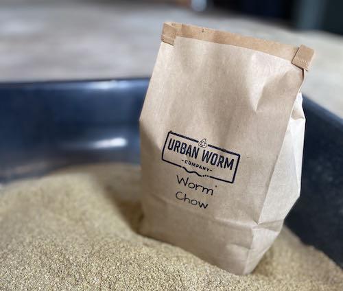 Bag of Urban Worm Chow protein-rich worm food next to worm feed in a mixing tray, ready for composting worms and vermicomposting systems.
